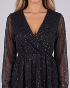 Close-up of the wrap V-neckline, sheer sleeves and glitter fabric of the black mini dress
