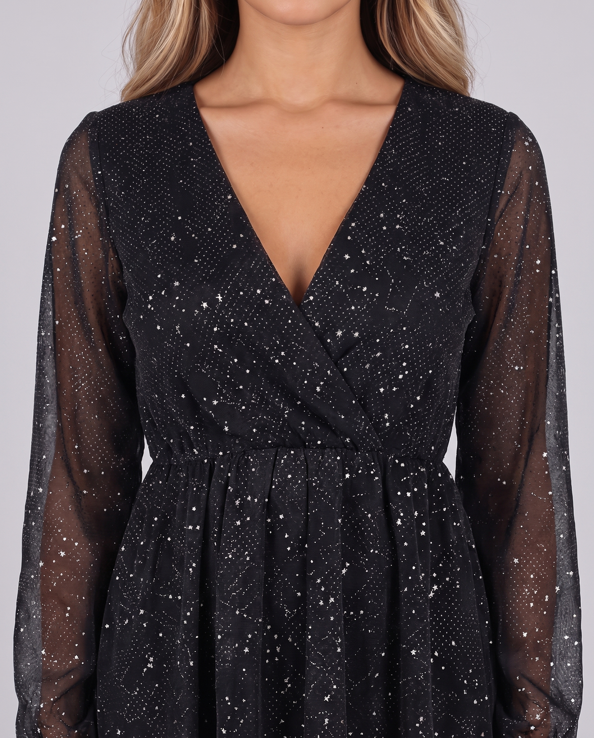 Close-up of the wrap V-neckline, sheer sleeves and glitter fabric of the black mini dress